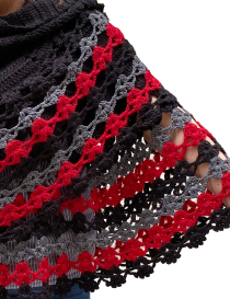 Front view of model wearing a black crochet cape with red and grey accents.