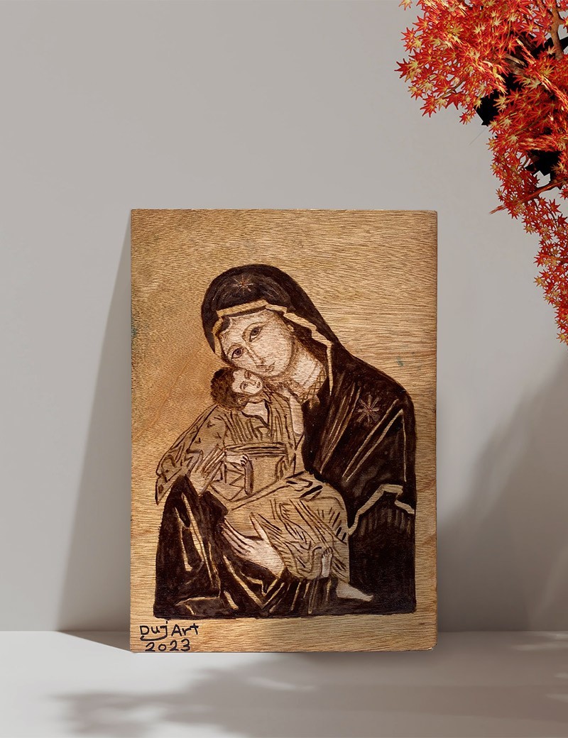Virgin Mary woodburned art on display with autumn leaves.