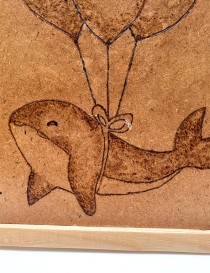 Detailed view of a smiling woodburned dolphin and ribbon knot.