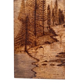 Detailed pyrography showing pine trees and mountain peaks etched into wood.
