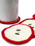 Close-up detail of crochet apple slice coaster showing red border and black seeds.