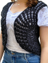 Close-up of a woman wearing a black crochet sleeveless vest over a white blouse.