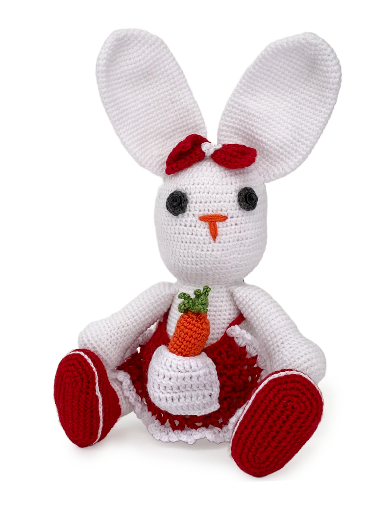 Front view of handmade white crochet rabbit in red apron holding a carrot.