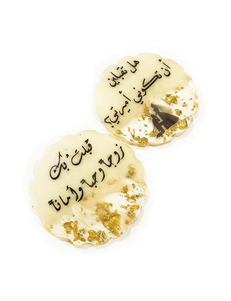 Set of two cream-colored resin marriage coasters with proposal silhouette and gold accents.