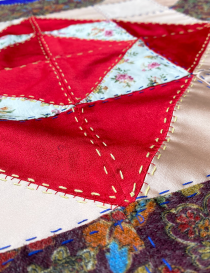 Detail of intricate needlework on red and gold satin fabrics.