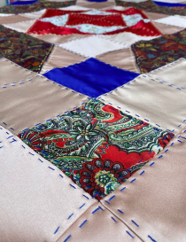 Close-up of blue and yellow hand-stitched embroidery on satin and paisley patches.