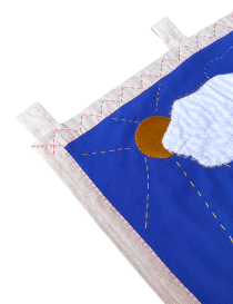 Top corner of the tapestry showing fabric hanging loops and sun embroidery.