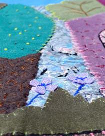 Close-up of delicate purple fabric flowers and intricate needlework on the tapestry.
