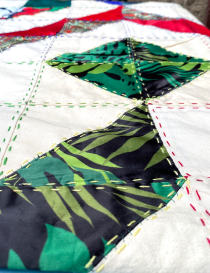 Detail of green and black palm leaf embroidery on raw fabric base.