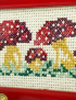 Close-up of handmade cross-stitch embroidery detail showing red and purple mushrooms.