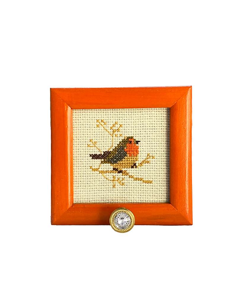 Front view of a square orange wooden frame with bird cross-stitch and a crystal hook.