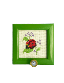 Front view of handmade ladybug cross-stitch embroidery in green frame with crystal hook.