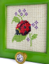 Close-up of ladybug needlepoint detail and decorative crystal hook on green frame.