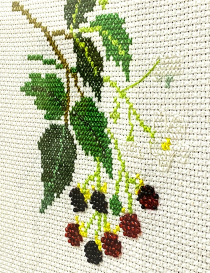 Close-up of green and red thread embroidery stitches on cream fabric.