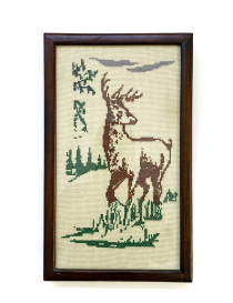 Front view of a framed handmade cross-stitch featuring a majestic deer and forest greenery.