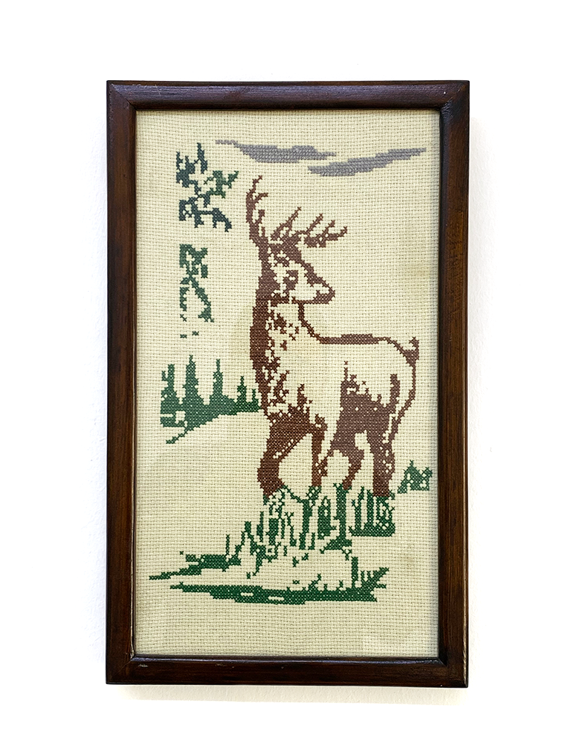 Front view of a framed handmade cross-stitch featuring a majestic deer and forest greenery.