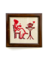 Front view of framed red cross-stitch of a woman drinking tea.