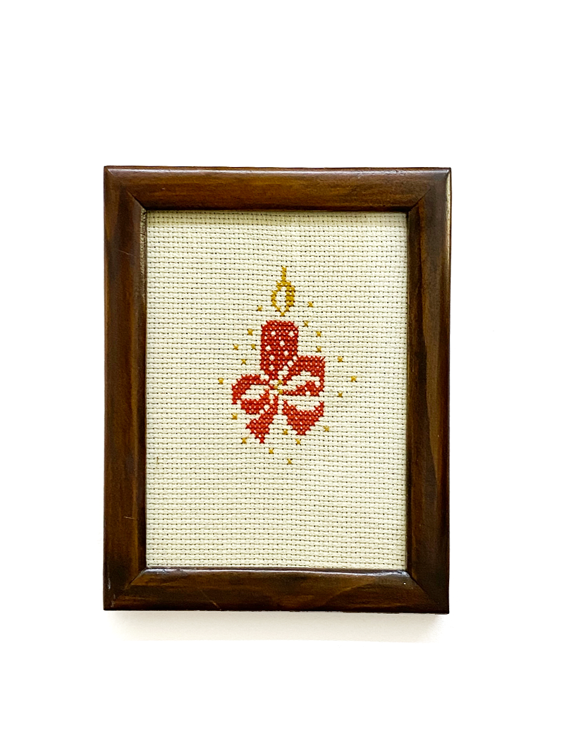 Front view of a framed red candle cross-stitch art with a dark wood frame.