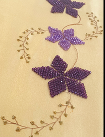 Close-up of intricate hand-stitched purple beads and copper wire vines.