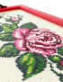 Detailed close-up of intricate rose blossom needlework and green leaf stitching.