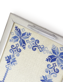 Close-up of blue cross-stitch embroidery and silver handle on wooden serving tray.