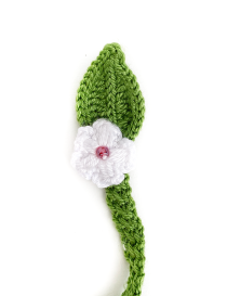 Close-up of a white crochet flower with a pink bead center on a green knitted leaf.