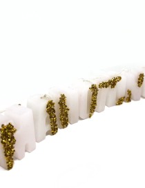 White wax letter candles with gold glitter accents spelling out a word on a white surface.