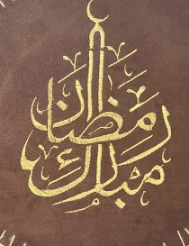 Circular brown suede wall hanging with gold "Ramadan Mubarak" mosque-shaped embroidery in a wooden hoop.