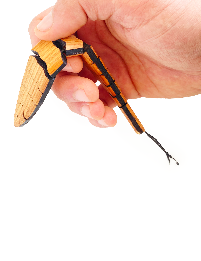 A hand holding the wooden fish to demonstrate its flexible, bending movement.