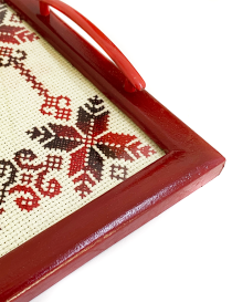 Close-up detail of red and black cross-stitch needlework and the polished burgundy wood frame.