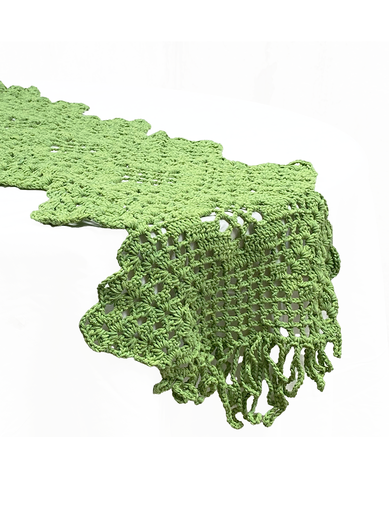 Close-up of green leaf crochet table runner draped over a table edge with fringe detail.