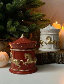 Deep red carousel horse candle with gold detailing placed next to a Christmas tree.