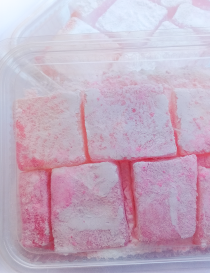 Clear plastic packaging container filled with fresh pink saffron sweets for Syrian local delivery.