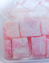 Clear plastic packaging container filled with fresh pink saffron sweets for Syrian local delivery.