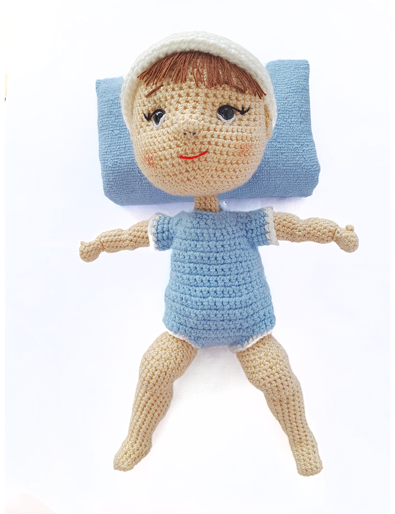 Full body view of Nano handmade crochet doll wearing a blue outfit with blue pillow