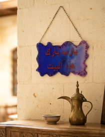 The resin blessing plaque hanging on a stone wall inside a warm, traditional Syrian home entrance.