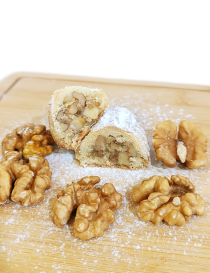 Cross-section of Syrian walnut maamoul showing generous walnut filling and powdered sugar on wooden board