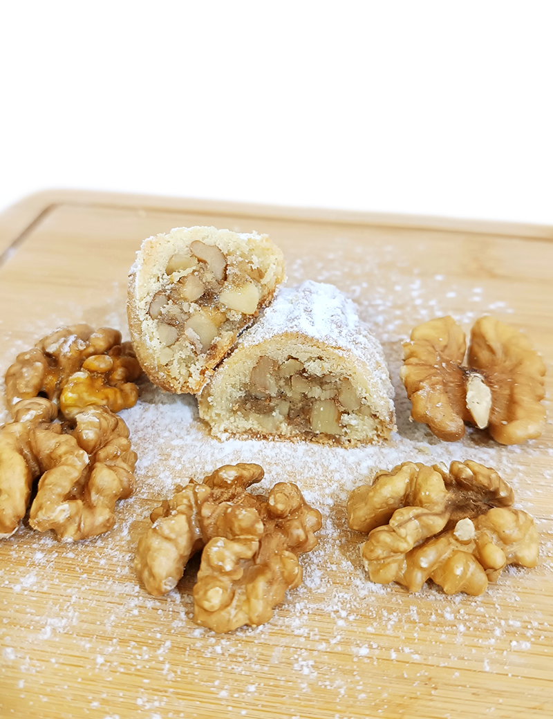 Cross-section of Syrian walnut maamoul showing generous walnut filling and powdered sugar on wooden board