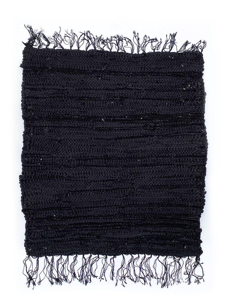 Flat lay of a hand-loomed recycled black fabric rug with fringe.