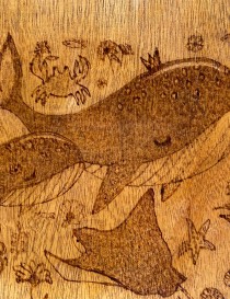 Close-up of woodburned whale and crab details.