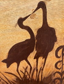 Close-up of pyrography detail showing the textured wood grain and charred bird silhouettes.