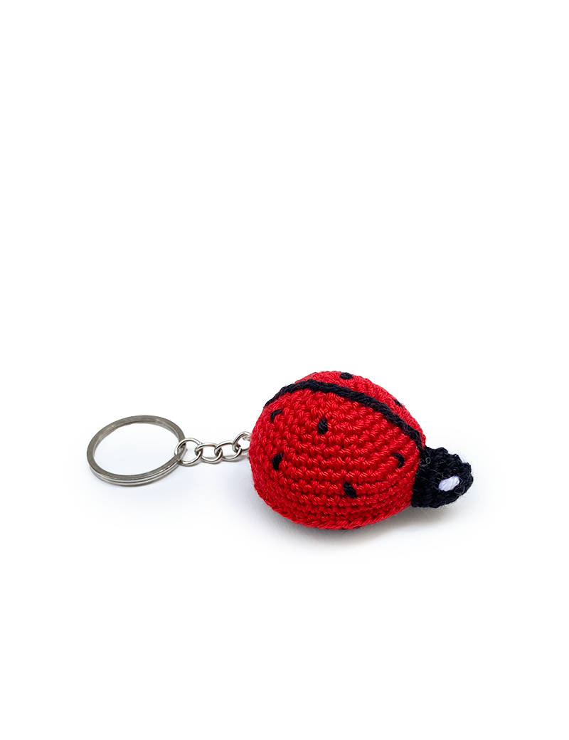 Side view of a red crochet ladybug keychain with black embroidered spots.
