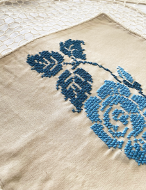 Detailed view of the blue rose cross-stitch embroidery on beige canvas.
