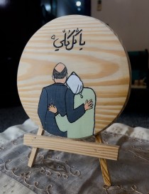 Hand-painted wood slice with hugging couple illustration and Arabic text "You are my everything" on easel.