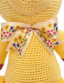 Close-up of a floral print cream bow tied around a yellow crochet bear's neck.