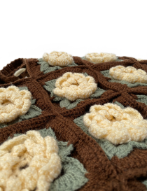 Close-up of 3D crochet roses and sage green leaves on a knitted brown background.