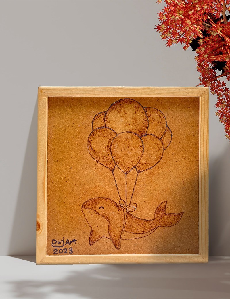 Framed woodburned art of a dolphin tied to balloons in a lifestyle setting.