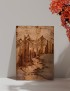 A4 woodburning art of a mountain landscape leaning against a white wall with autumn leaves.