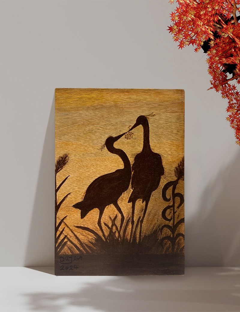 Silhouette woodburning of two birds on a wooden panel standing against a neutral wall.