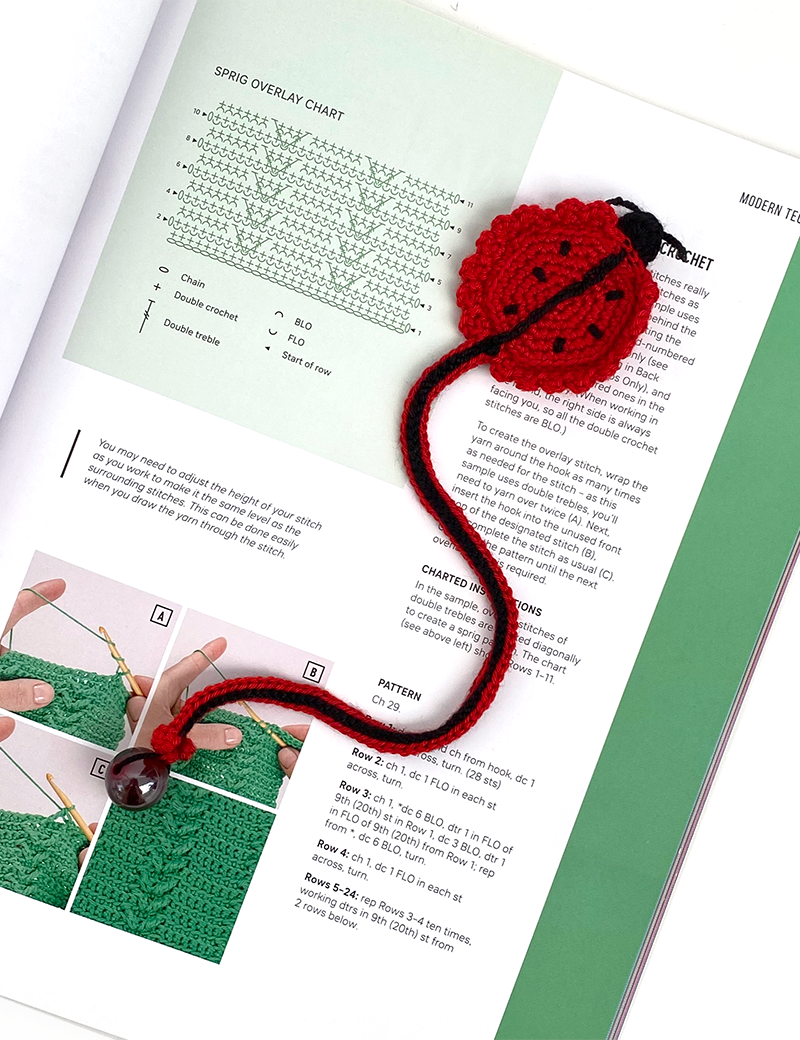Red and black crochet ladybug bookmark resting on an open page of a craft book.